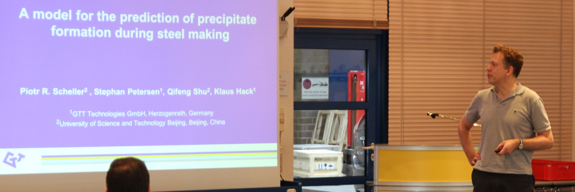 A photo from the Users' Meeting Archive 2016 shows CEO Stephan Petersen presenting a slide titled 'A model for the prediction of precipitate formation during steel making.' The slide lists the authors and their affiliations, including GTT-Technologies GmbH and the University of Science and Technology Beijing. Stephan Petersen stands to the right, holding a pointer, in a classroom setting.