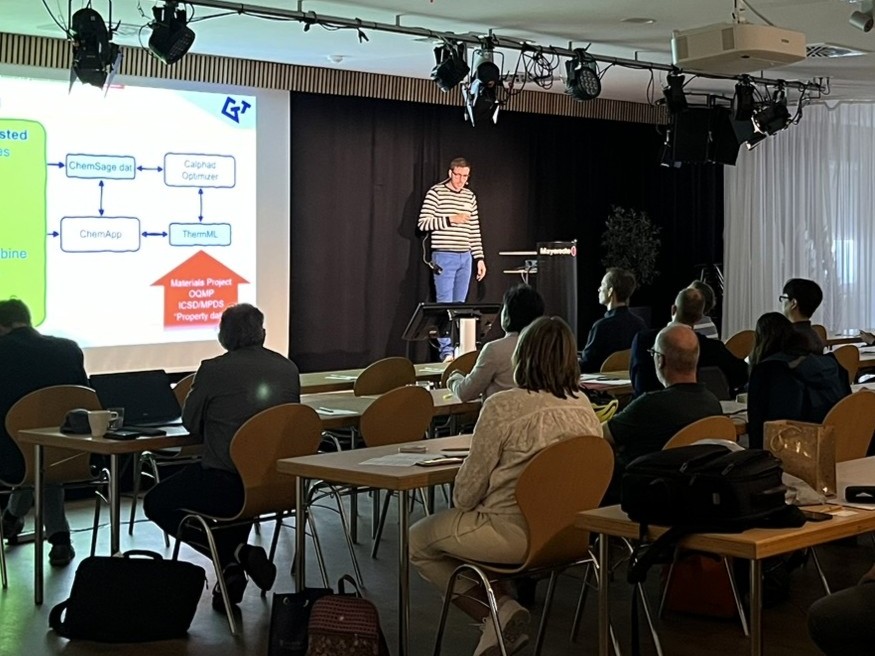Speaker presenting technical software workflows during a Users’ Meeting conference session, with attendees seated in the audience and presentation slides displayed on a large screen.